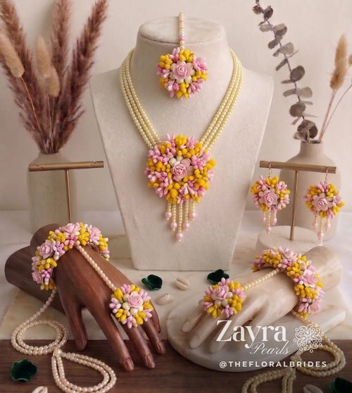 Handcrafted pink and yellow Haldi Canival Jewelry for brides set with a multi-strand pearl necklace, floral accents on a mannequin and hands, featuring Zayra Pearls 