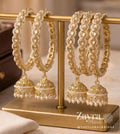 Zayra Pearls royal gold Kundan kangan bangles in a pair featuring hanging jhumkas bordered with tiny white seed pearls on a gold T-bar display
