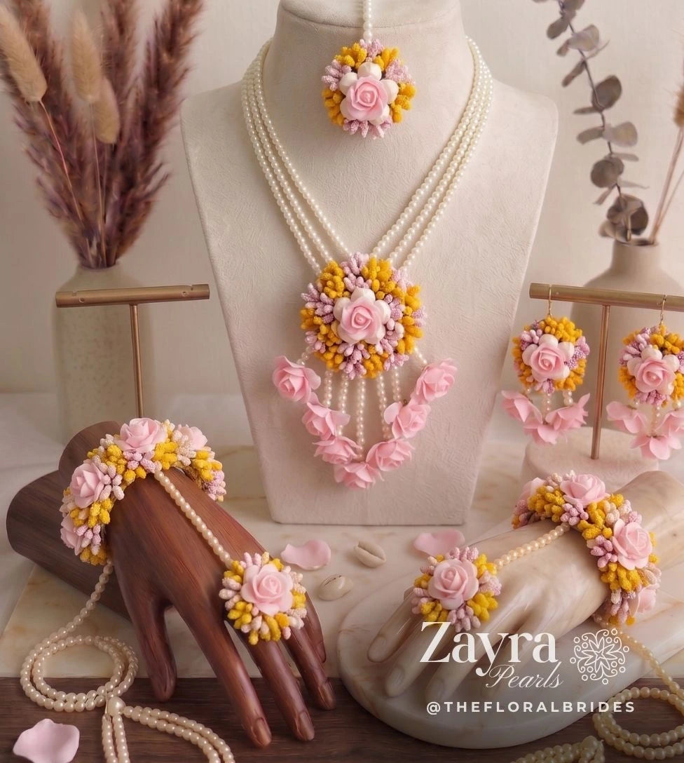 Handcrafted yellow and pink Pink Haldi Carnival Jewelry set with a multi-strand pearl necklace, matching maang tikka, earrings, and haathphools displayed on busts as seen featuring Zayra Pearls brand.
