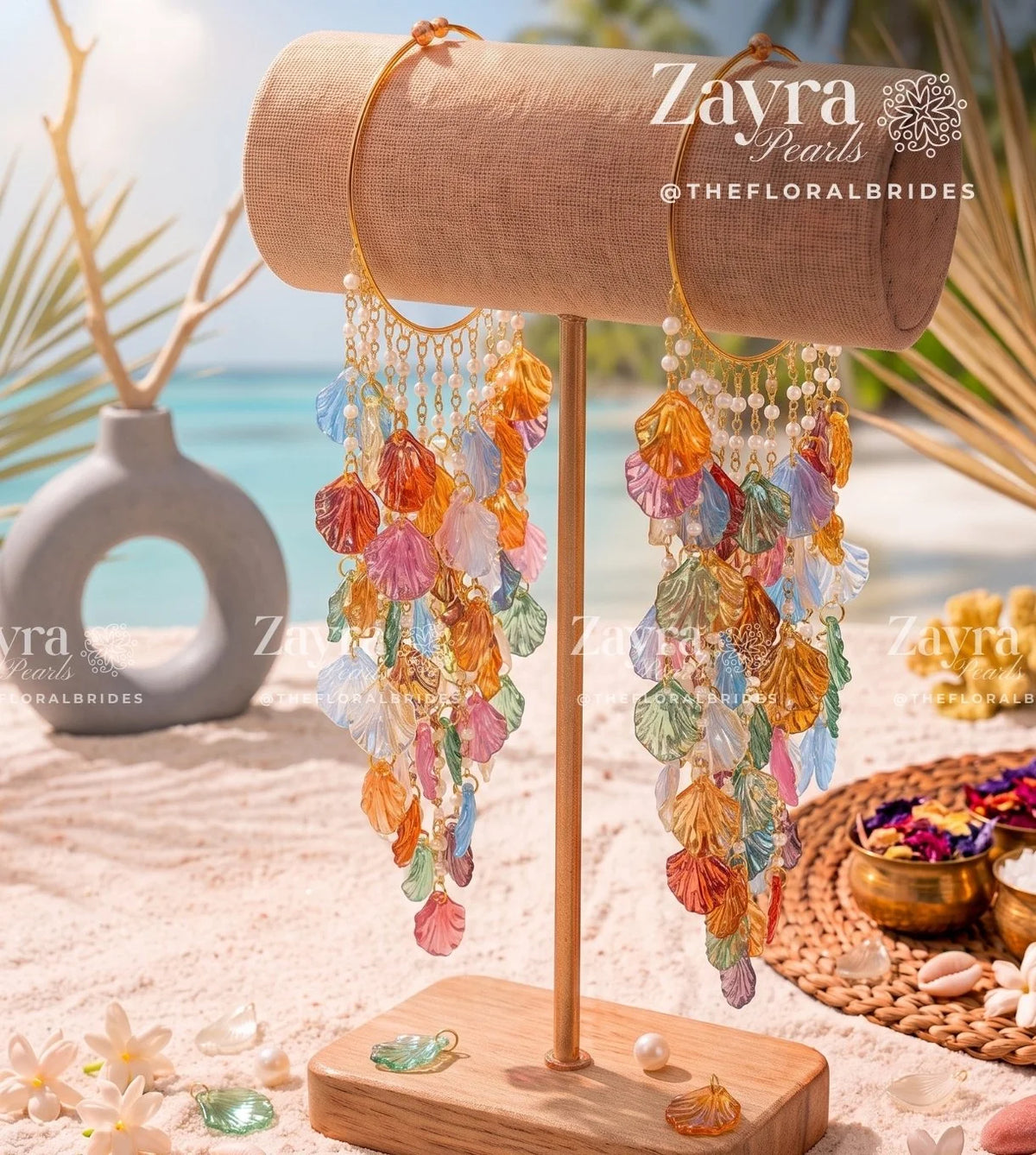 Colorful dangling earrings displayed on a wooden stand in a beach-themed setting with sand Handcrafted haldi carnival bangels with multicolor yellow blue pink and orange resin petals and cowrie by zayra pearls