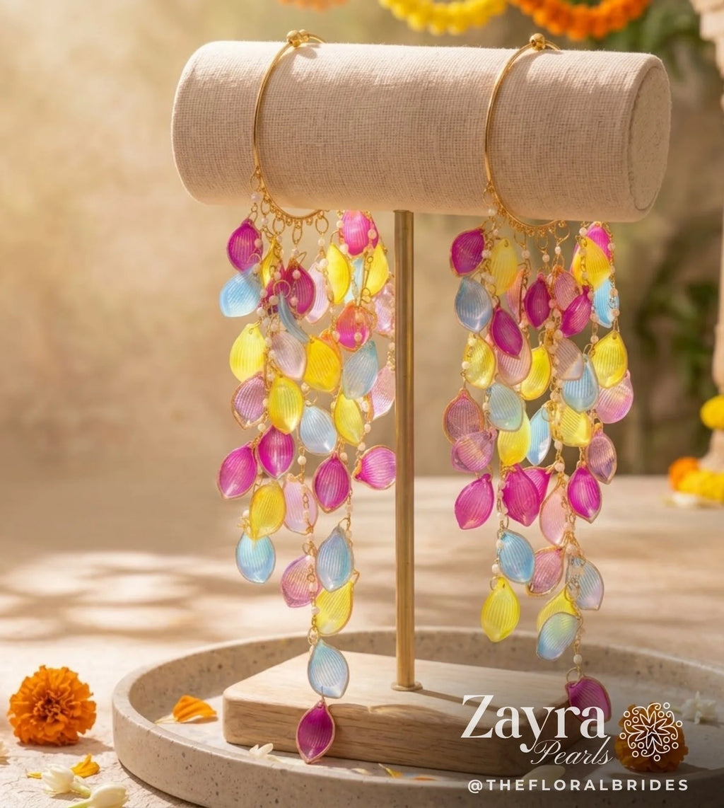 Zayra pearls Colorful dangle earrings with translucent teardrop-shaped beads in pink, yellow, and light blue, hanging from gold hoops on a beige jewelry display stand.