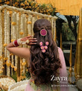 pink -Personalized Bridal Hair Accessory | Zayra Pearls woman shown from behind wearing a long, dark brown wavy hairstyle with a half-up bun, decorated with a pink circular hair pin and a floral hair clip. She is wearing a pink and green traditional outfit and has red and white bangles on her hand.