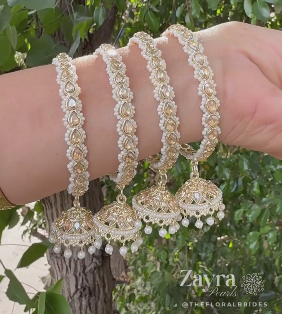 Zayra Pearls VIDEO for royal gold Kundan kangan bangles in a pair featuring hanging jhumkas bordered with tiny white seed pearls on a gold T-bar display