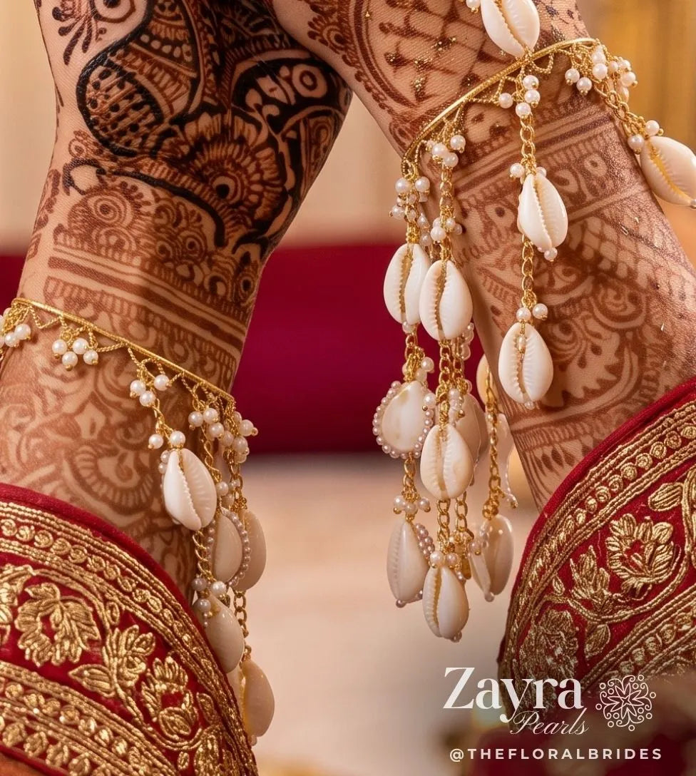 Close-up of a indian bride wearing Handcrafted shell kaliras for haldi & mehendi with cascading cowrie shells on gold hoop bangles by zayra pearls