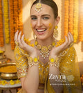 Woman in traditional yellow attire with yellow-kundan-haldi-set against a floral backdrop, featuring Zayra Pearls branding.