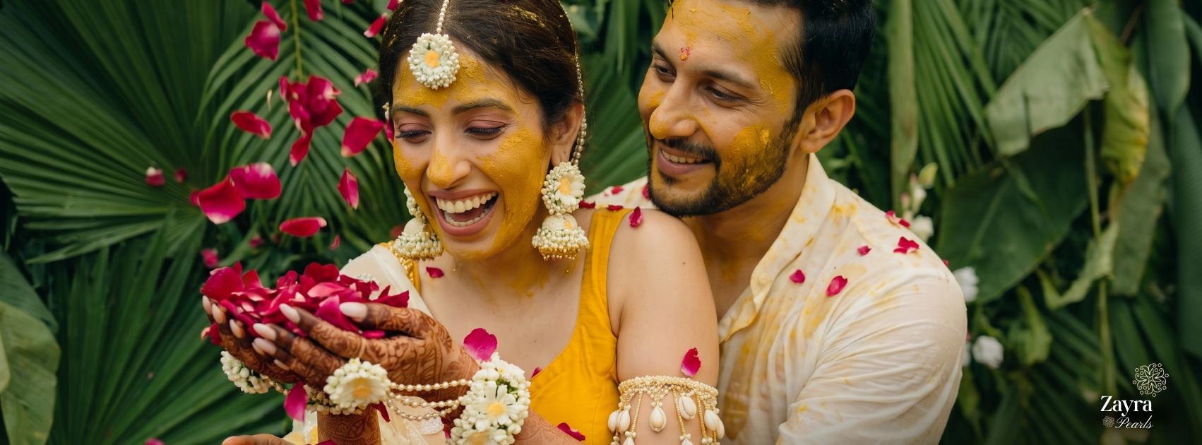 zayra pearls Couple in traditional attire with floral decorations amidst green foliage